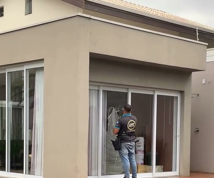 Profissional da equipe limpando a porta de vidro de uma casa, ao lado de um lago